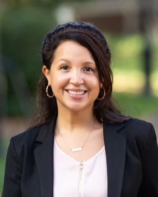A professional headshot of a woman with light brown skin and dark brown hair. She is looking at the camera and smiling.